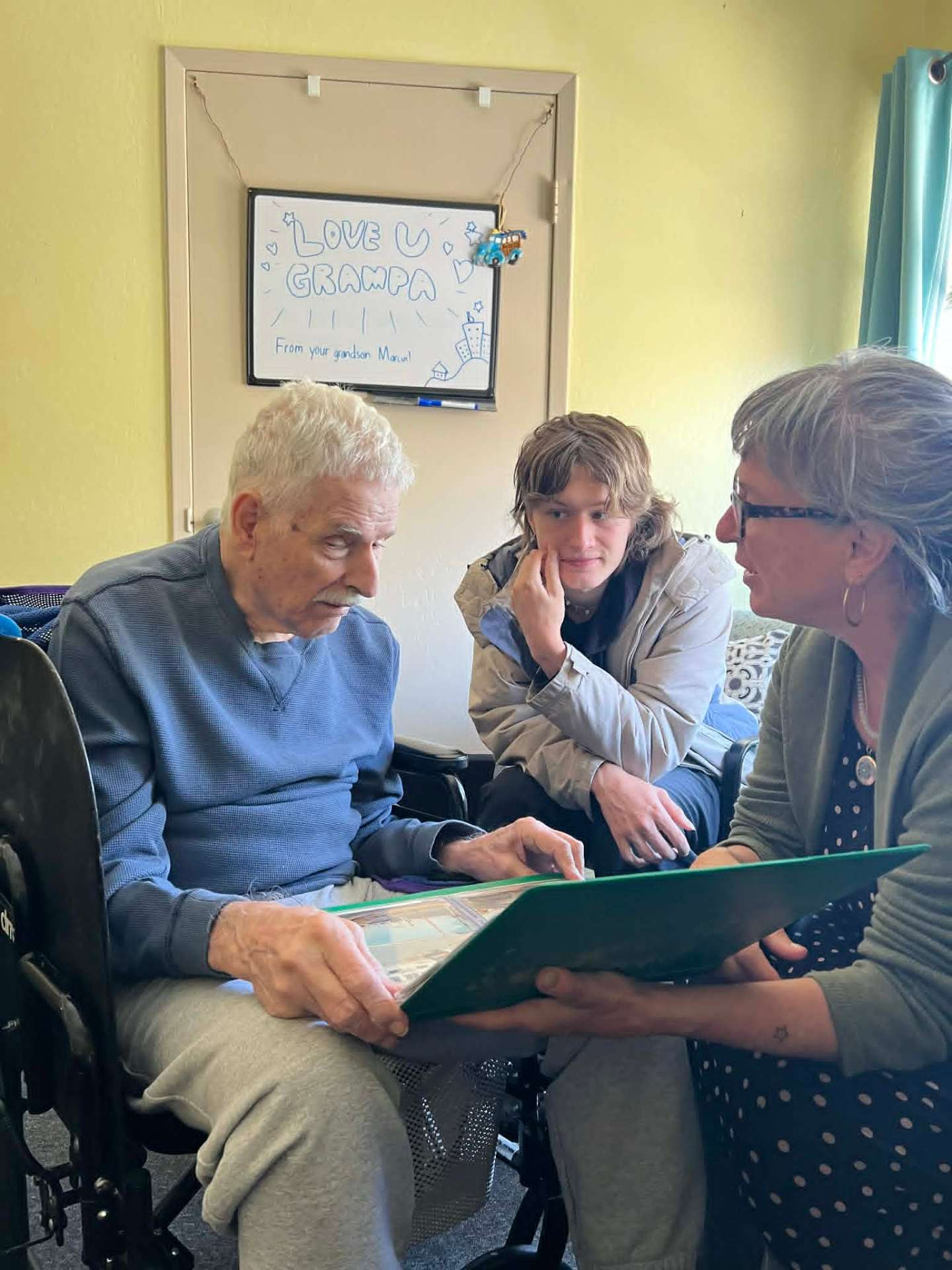 An elderly gentleman looking through a photo album with family visiting him at home