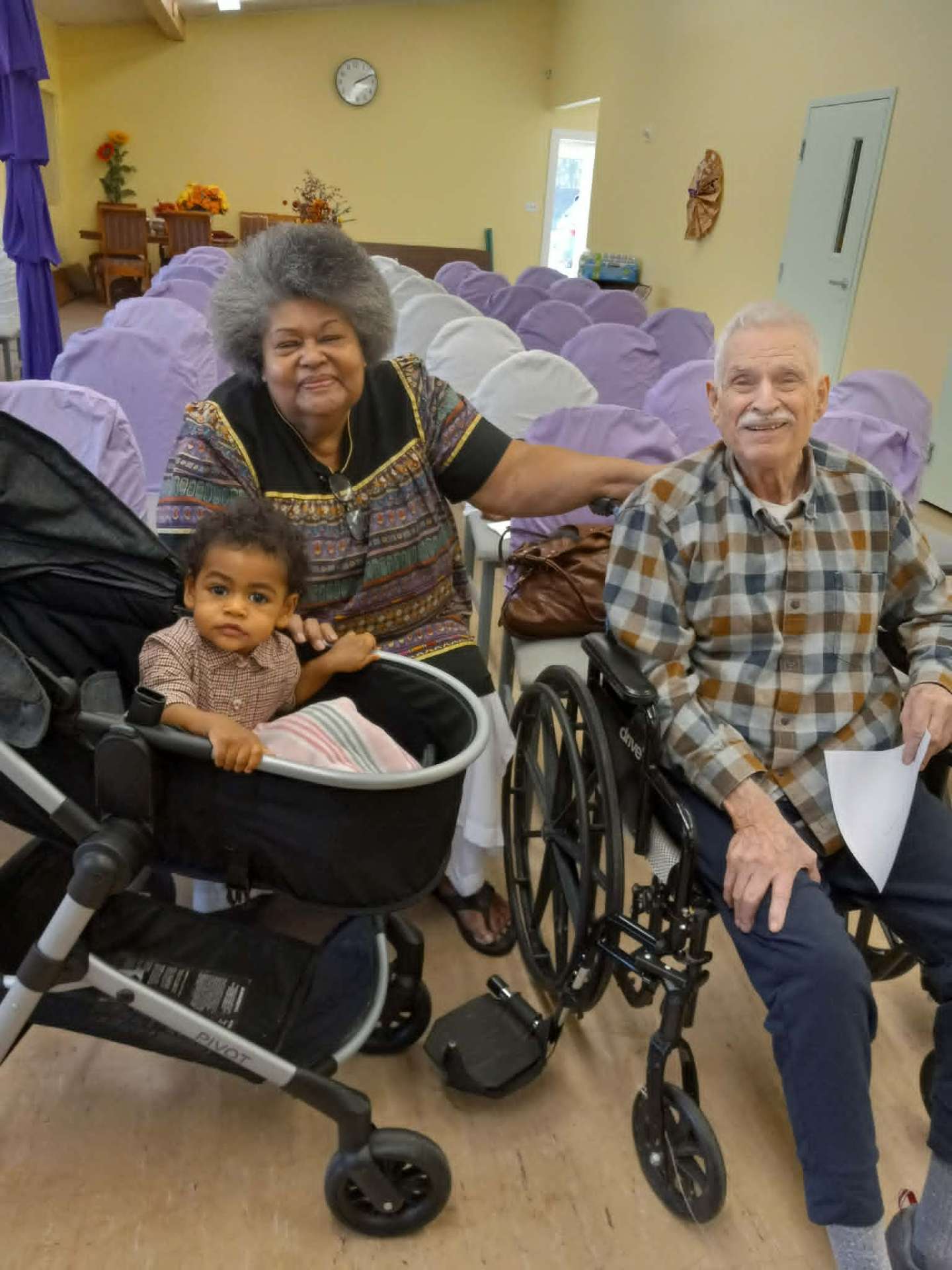 A caregiver, an elderly gentleman in a wheelchair and a young child together in a bright community room